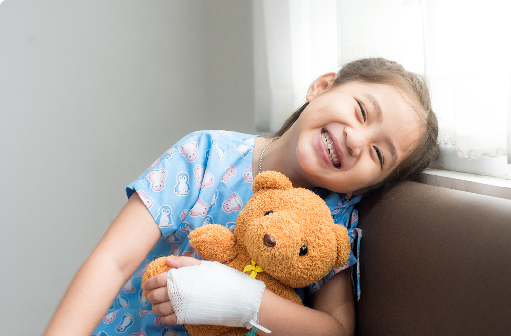 Image is of a young girl holding a teddy bear smiling towards the camera